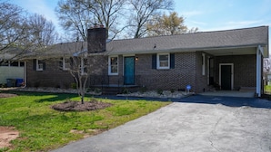 A single-story brick house with a front porch, a small tree, and a driveway.