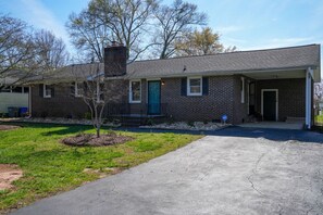 A single-story brick house with a front porch, a small tree, and a driveway.