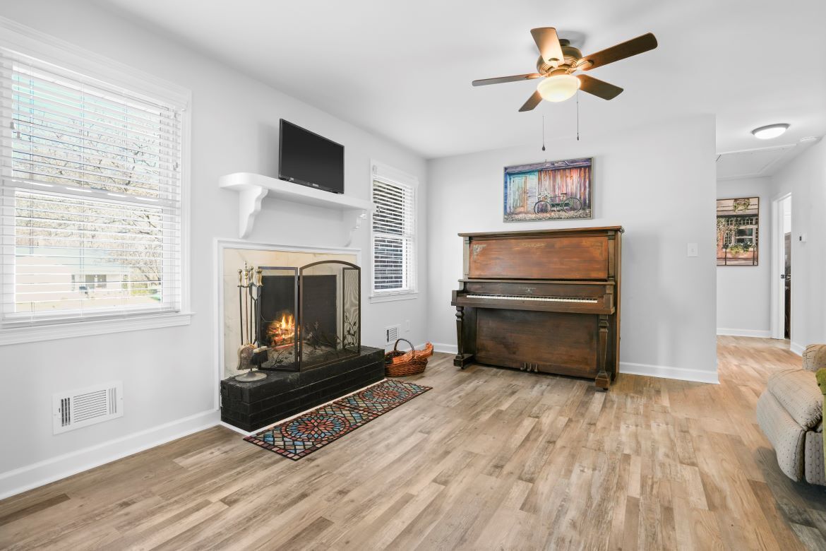 A living room with a fireplace, a piano, a ceiling fan, and a television.