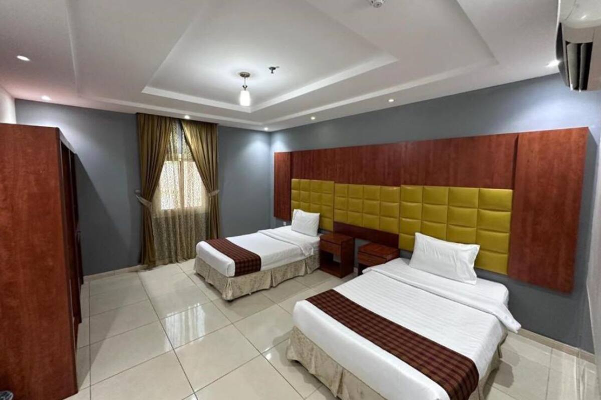 A hotel room with two beds, a wooden wardrobe, a window with curtains, and a ceiling light.