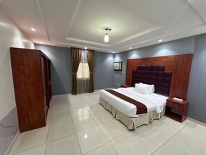 A hotel room with a large bed, a nightstand, a wooden headboard, a ceiling light fixture, and a window with curtains. - Furnished apartments (Jeddah)
