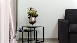 Ein modernes Zimmer mit einem schwarzen Metall-Nachttisch, einer Vase mit Blumen, einem kleinen Behälter und einem schwarzen Ledersessel.