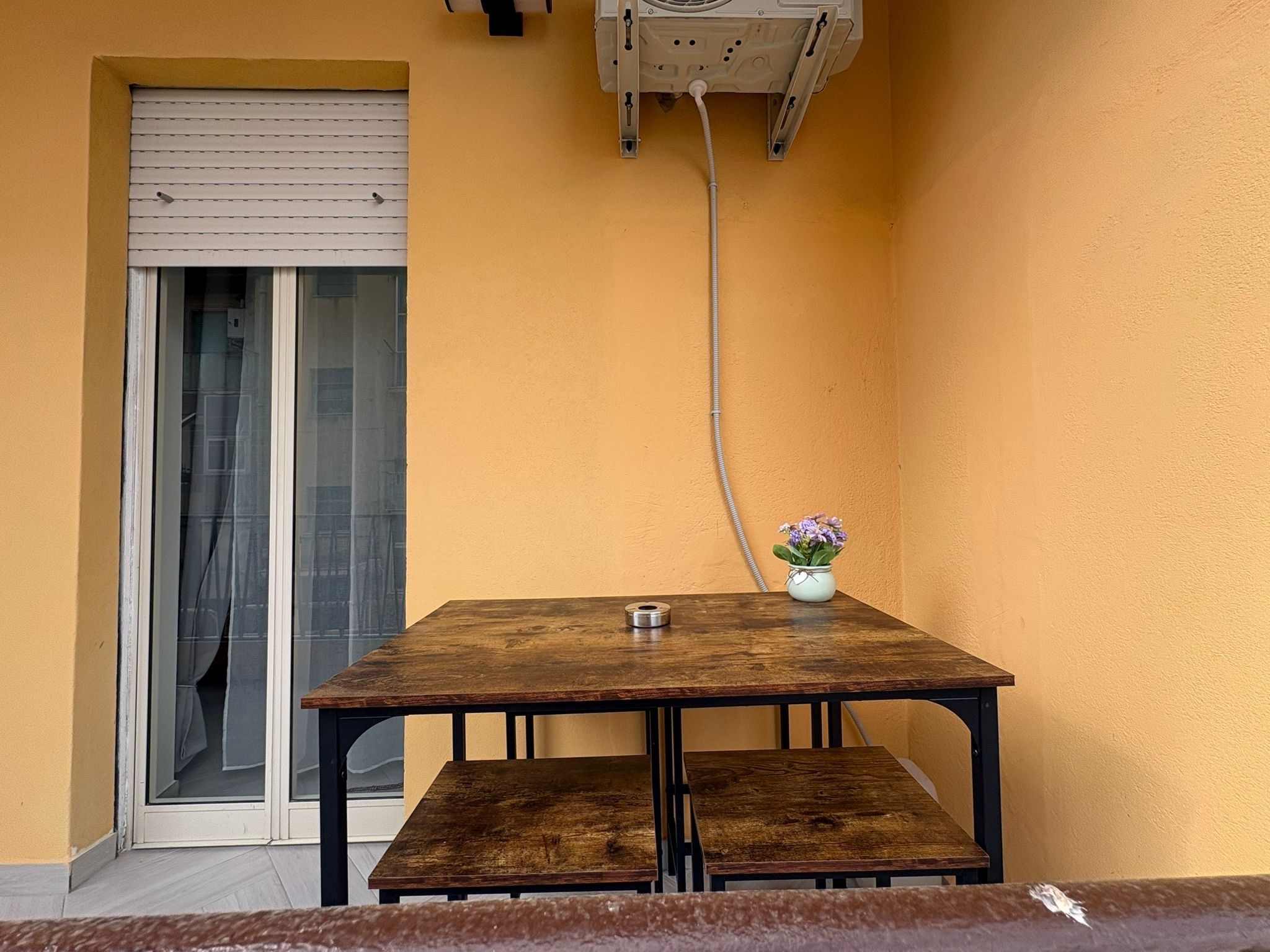 A small outdoor seating area with a wooden table and benches, a potted plant, and a sliding glass door.
