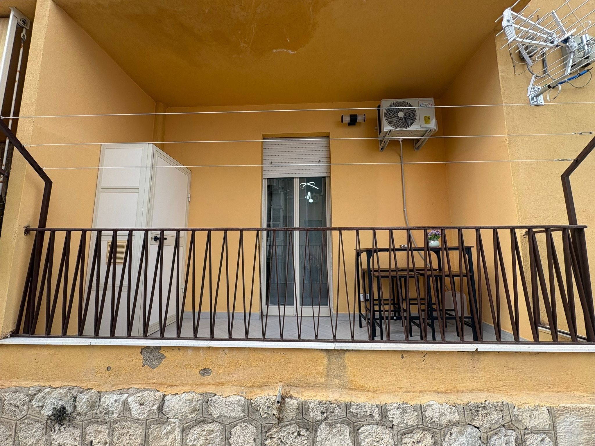 Un balcon avec une rambarde en métal, une porte et un appareil de climatisation.