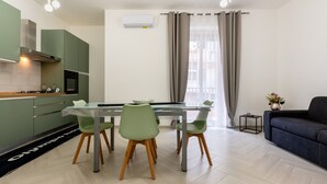 Eine moderne Küche mit grünen Schränken, einem Esstisch mit Stühlen, einer Couch und einem kleinen Beistelltisch mit einer Pflanze.
