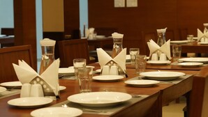 Un comedor con mesas de madera dispuestas para una comida, con platos, vasos y servilletas.
