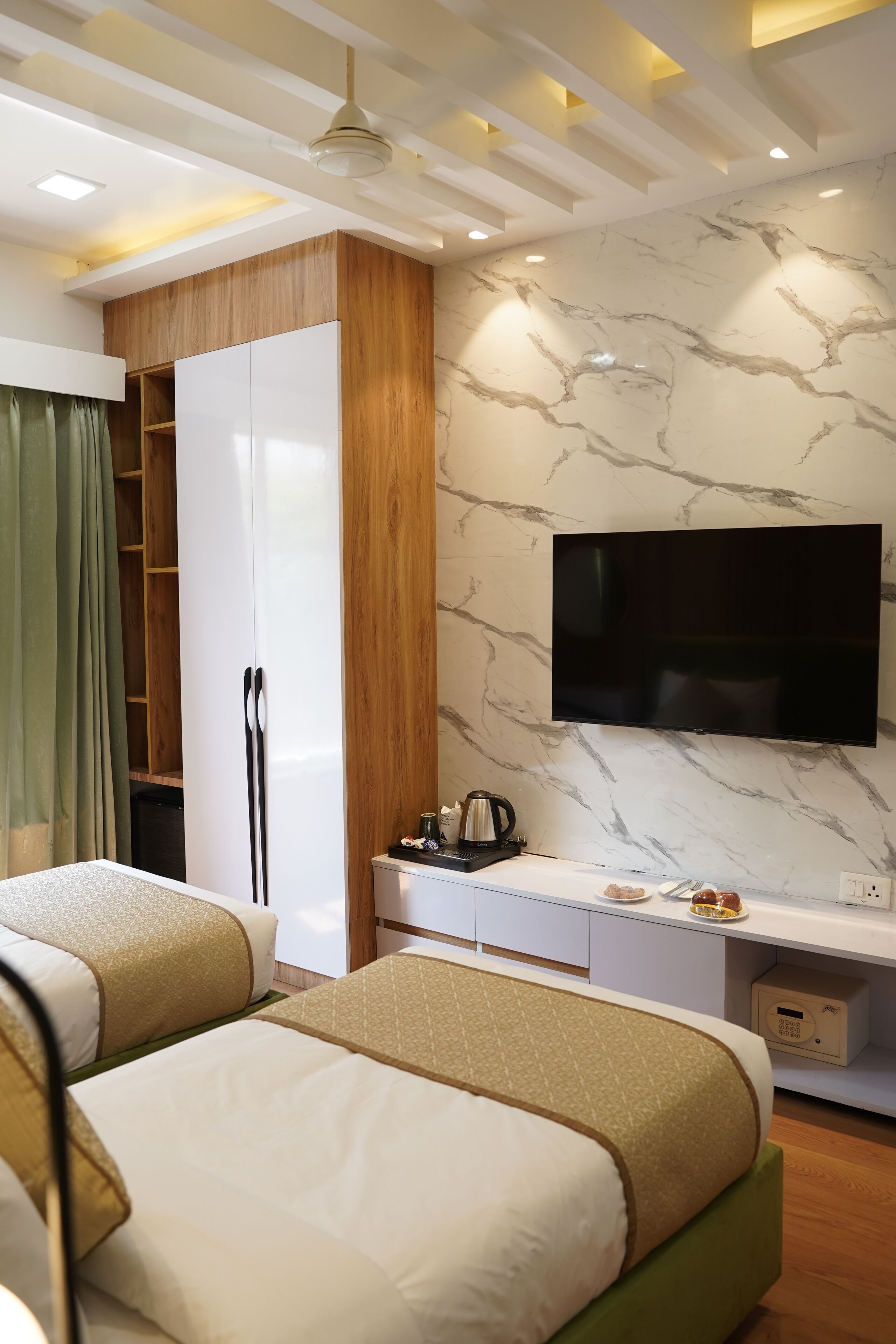 A hotel room with two beds, a TV, a wardrobe, and a desk with a coffee maker.