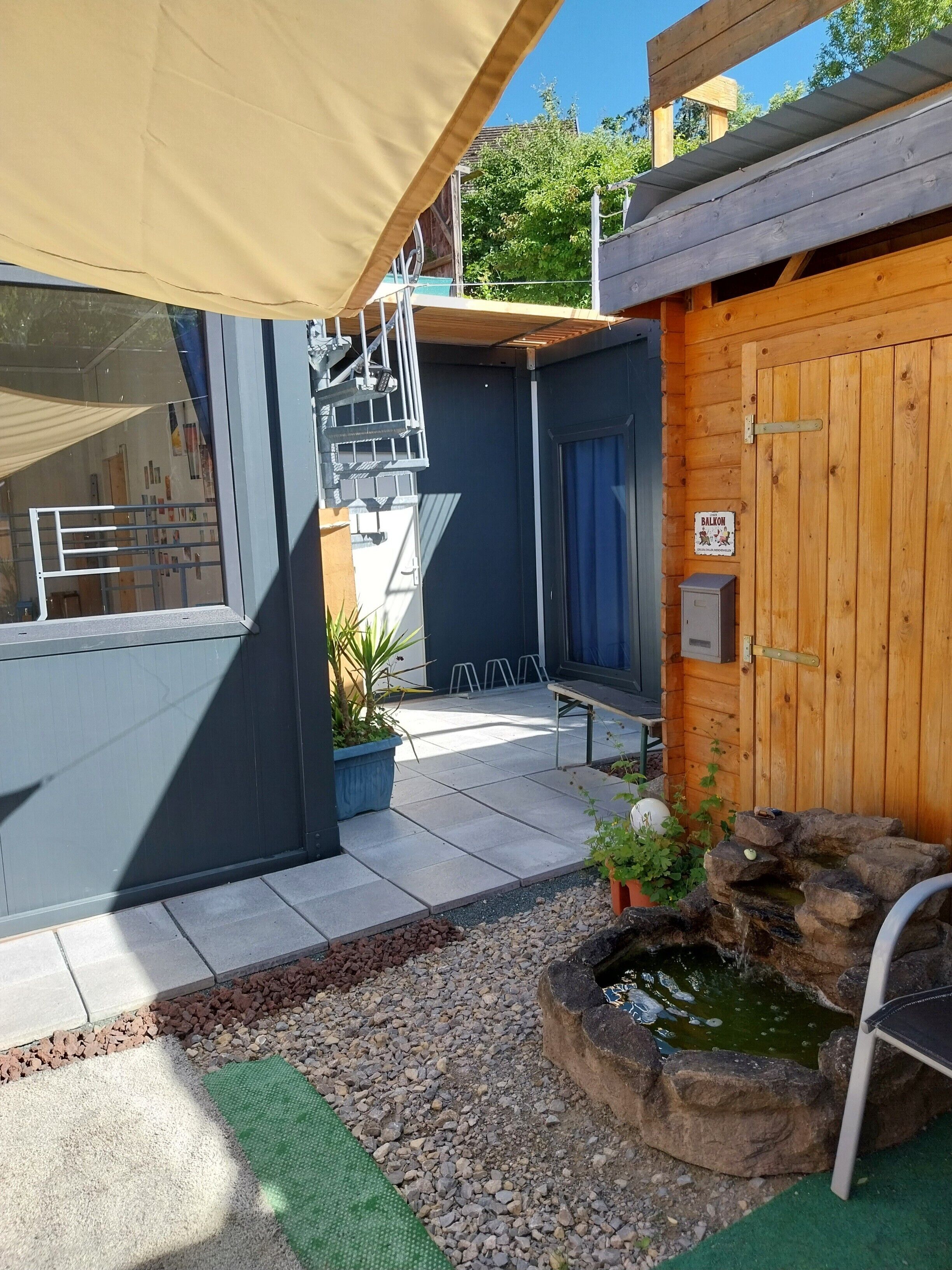 En byggnad av trä med en skylt på balkongen, en täckt uteplats och en liten fontän eller liknande vattenelement.