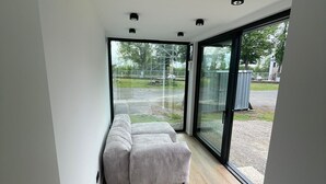 En modern inredning med en stor skjutdörr i glas som leder ut till ett utomhusområde, ett trägolv och en sektionssoffa.