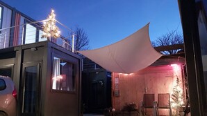 En byggnad med en täckt uteplats, en parkerad bil utanför och en träkonstruktion med en dörr.