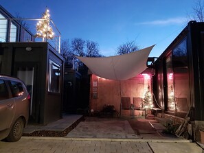 Un bâtiment moderne doté d’un espace extérieur couvert, une voiture garée devant, et une structure en bois sur laquelle est installé un sapin de Noël.