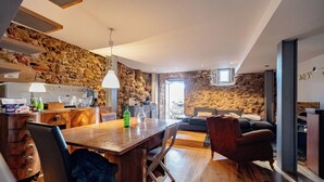 A modern kitchen with stone walls, wooden flooring, a dining table with chairs, and a cozy living area with a sofa and a fireplace. - The Balcony of Time - archaeology and history - charming central place wth terrace (Coimbra)