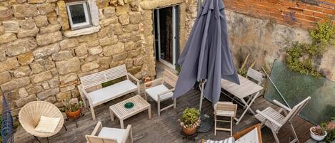 A wooden deck with outdoor furniture, a stone wall, and a brick building.