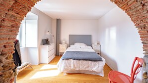 A bedroom with a brick archway, a bed with white bedding, a red chair, and a desk with a lamp. - The Balcony of Time - archaeology and history - charming central place wth terrace (Coimbra)