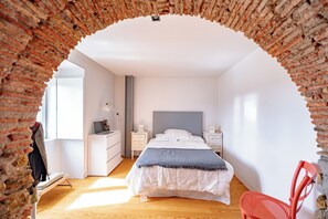 A bedroom with a brick archway, a bed with white bedding, a red chair, and a desk with a lamp. - The Balcony of Time - archaeology and history - charming central place wth terrace (Coimbra)