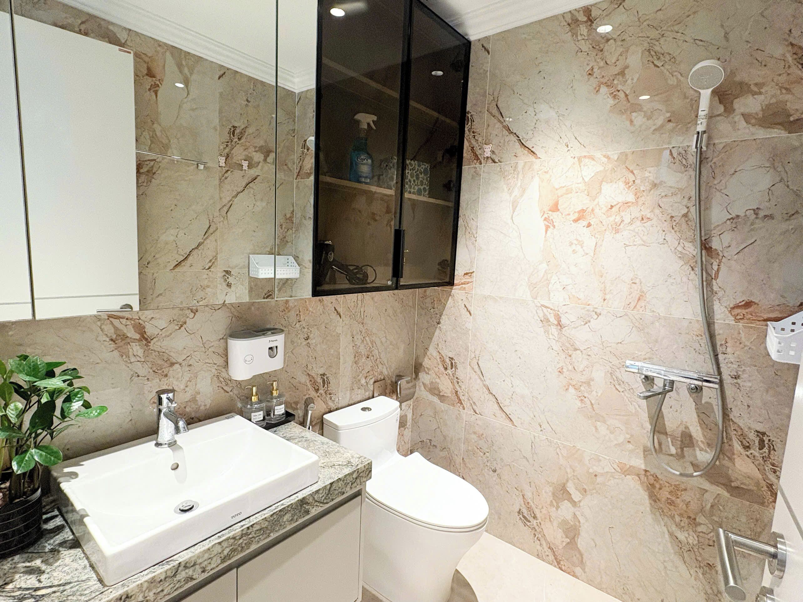 A modern bathroom with a marble backsplash, a white sink, a toilet, and a shower with a handheld showerhead.