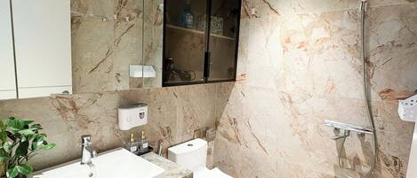 A modern bathroom with a marble backsplash, a white sink, a toilet, and a shower with a handheld showerhead.