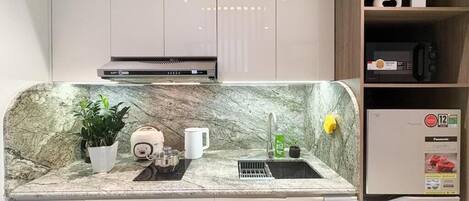 Une cuisine moderne dotée d’un plan de travail en marbre, d’une cuisinière encastrée et d’un évier. On y trouve des placards au-dessus du plan de travail et une étagère où sont disposés des objets décoratifs.