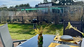 Mesa de comedor al aire libre con vistas a un patio trasero, una parrilla y una cerca de madera.