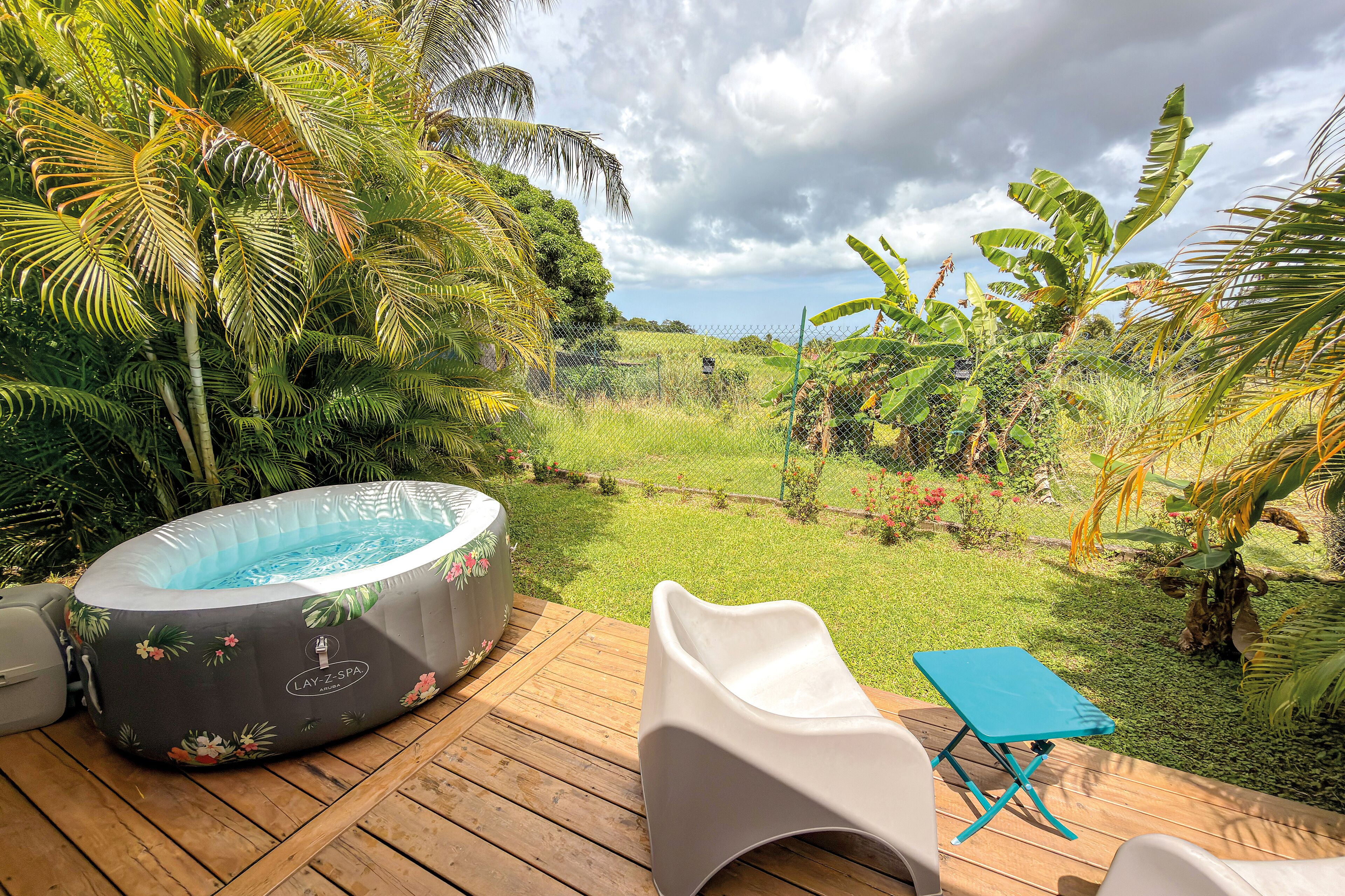 An outdoor hot tub on a wooden deck with a view of a lush garden and a grassy field.