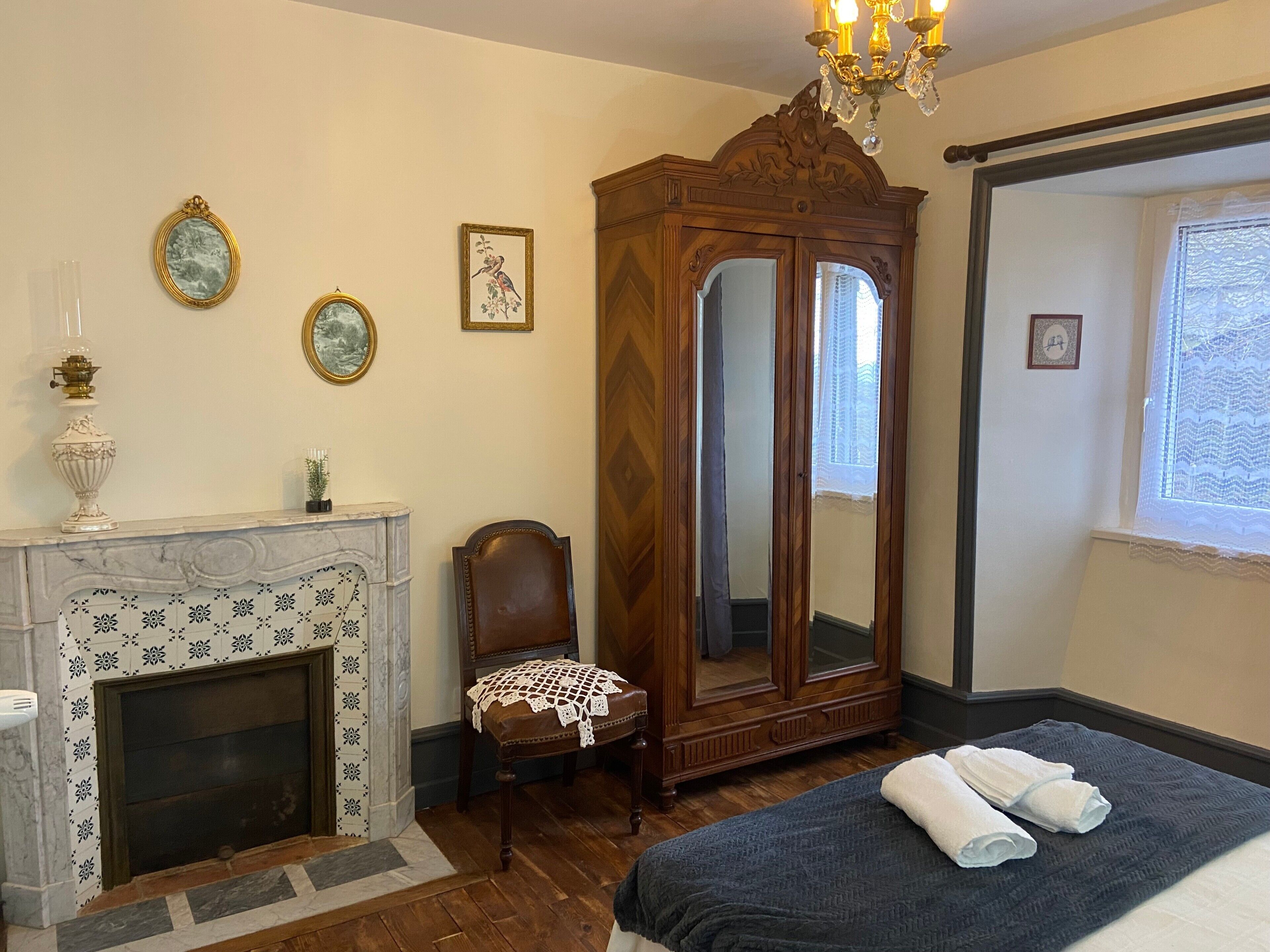 Une chambre avec une cheminée, un grand miroir, un lit avec des serviettes et une armoire en bois.