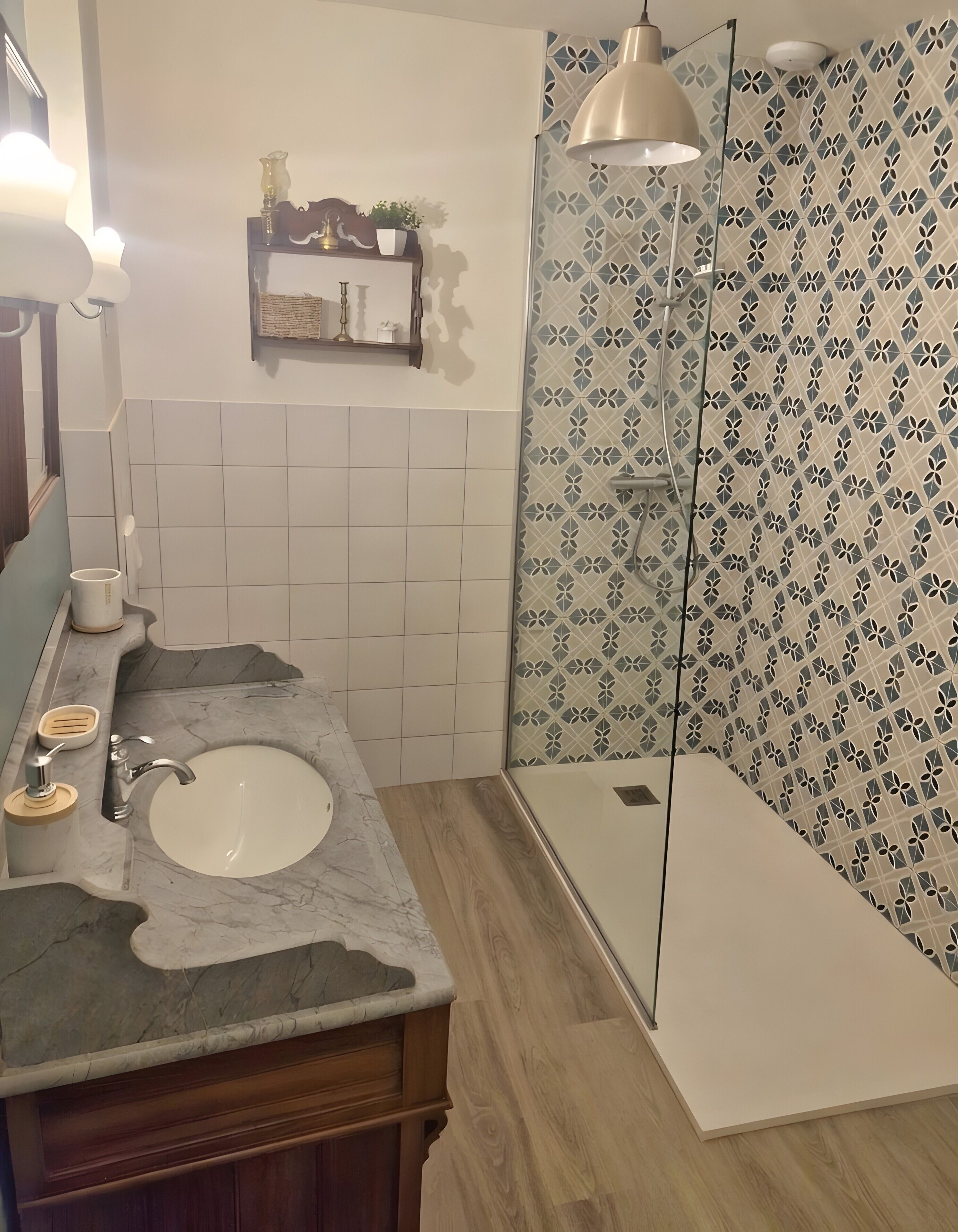 A bathroom with a marble sink, wooden vanity, a shower with a patterned wall, and a pendant light.