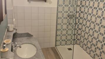 Un baño con lavamanos de mármol, tocador de madera, ducha con pared estampada y lámpara colgante.