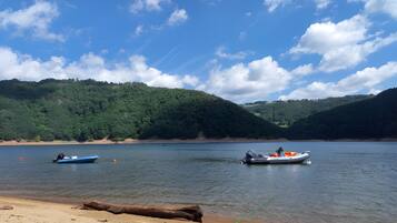 A calm lake with boats, a sandy beach, and forested hills in the background.