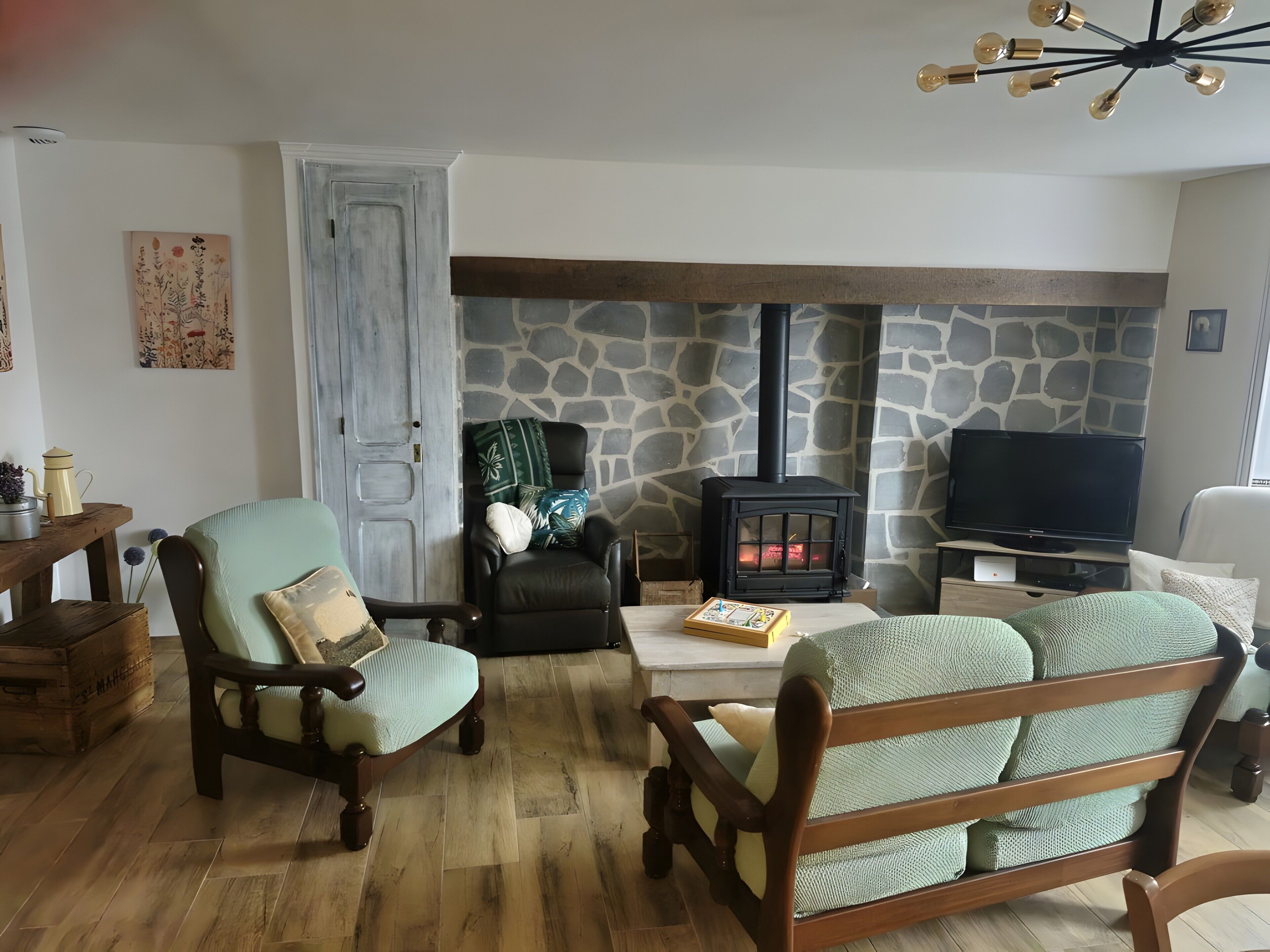 A cozy living room with a stone wall, a fireplace, a television, and wooden furniture.
