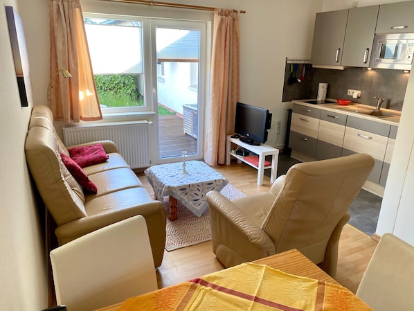 Una sala de estar con sofá, televisor, una mesita y una zona de cocina con alacenas y un microondas.