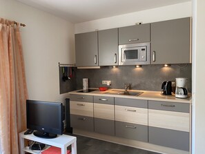 Una cocina compacta con microondas, cafetera y televisor sobre una mesita.