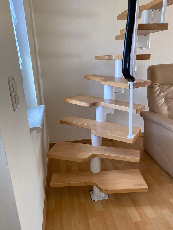 A multi-level cat tree with wooden platforms and a black scratching post in a room with a beige sofa and wooden flooring. - Apartment “Rudenblick” with Sea View, Private Terrace and Wi-Fi (Kröslin)
