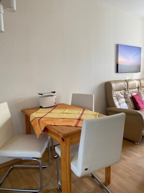 Un comedor con una mesa de madera, sillas blancas, un electrodoméstico blanco y un sofá color crema.