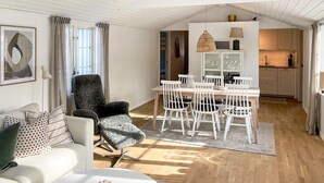 A modern living room with a sofa, a dining table with chairs, a kitchen area, and a large window. - 5 Star Holiday Home in Farjestaden (Farjestaden)