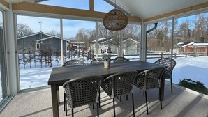 A covered patio with a table and chairs, large windows, and a view of a snowy landscape. - 5 Star Holiday Home in Farjestaden (Farjestaden)