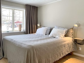 Une chambre avec un grand lit, une fenêtre avec des rideaux et une lampe fixée au mur.