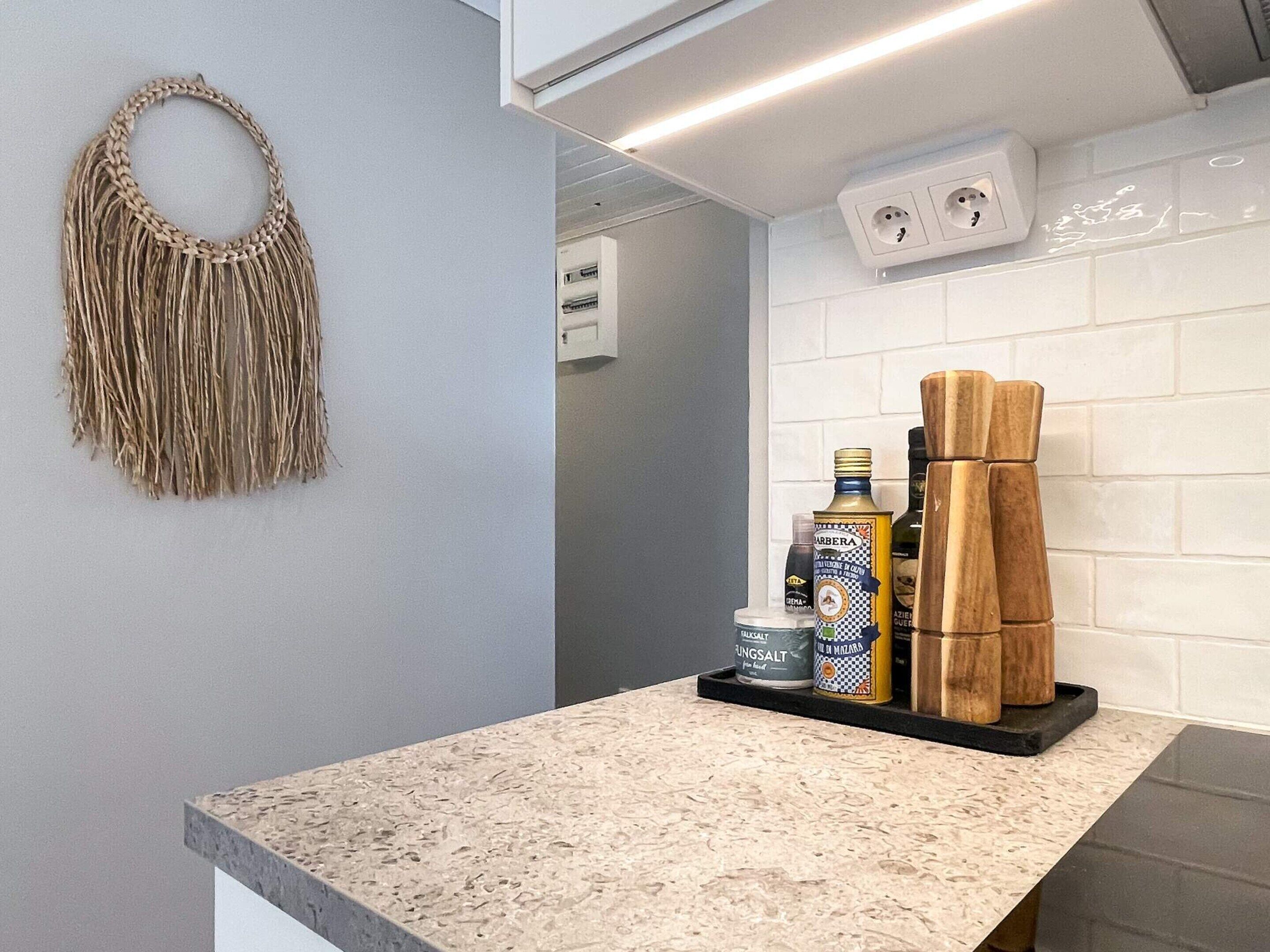 Eine Küche mit einer Granitabdeckung, einem gewebten Wandbehang und einem Regal mit Flaschen und Holzklötzen.