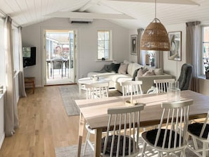 Un salon spacieux avec une grande table à manger en bois, des chaises blanches et un luminaire suspendu en fibres tressées.