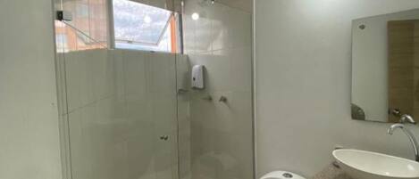 A bathroom with a glass shower enclosure, a toilet, a sink, and a red bucket.