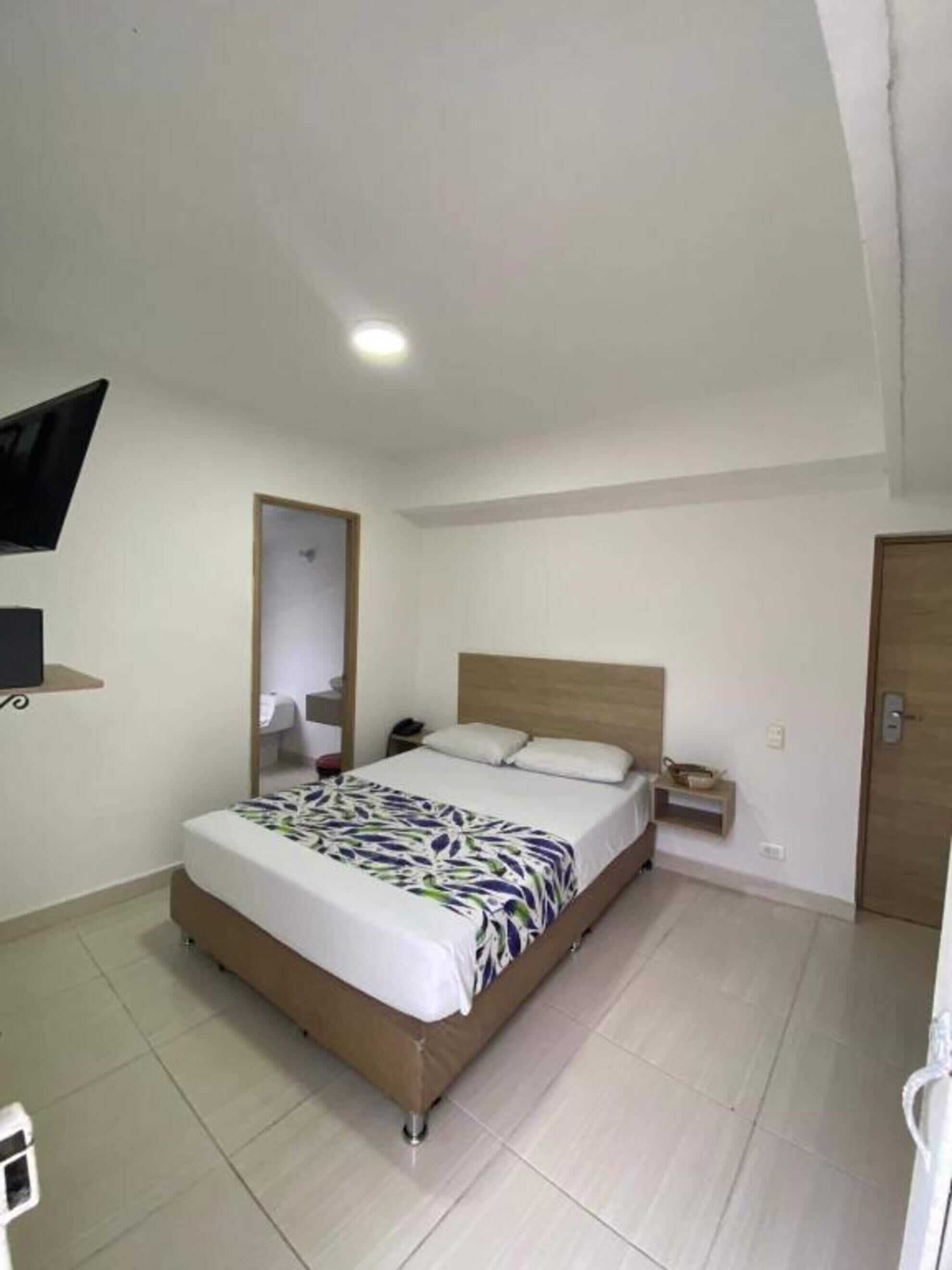 A bedroom with a bed, a bedside table, a nightstand, a TV mounted on the wall, and a door.