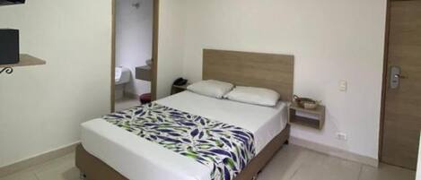A bedroom with a bed, a bedside table, a nightstand, a TV mounted on the wall, and a door.