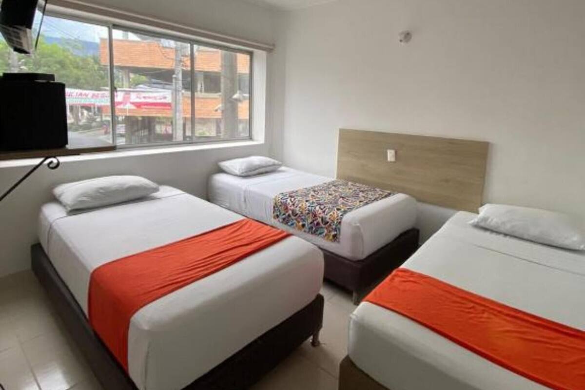 Een hotelkamer met drie bedden, een televisie en een raam met uitzicht op de straat.