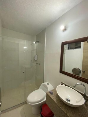 A bathroom with a glass shower enclosure, a toilet, and a sink with a mirror above it. - Hotel Suites 44 Laureles (Medellin)