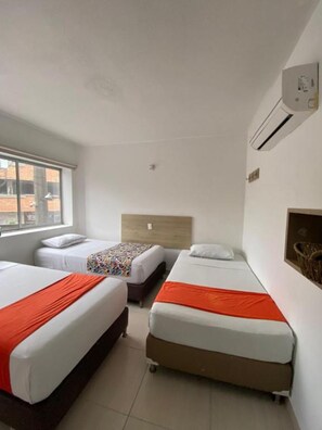 Een hotelkamer met drie bedden, een raam, een airconditioning en een wandplank.