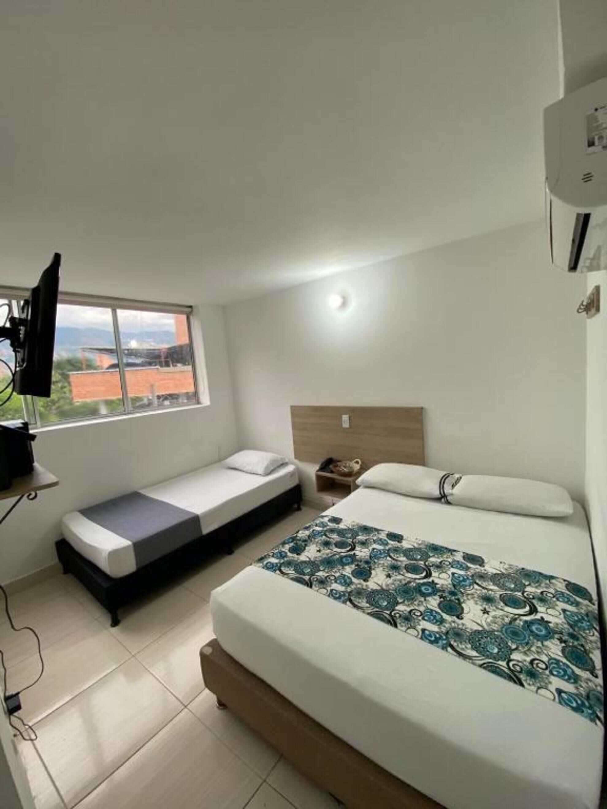Une chambre à coucher avec un lit, un banc, une télévision et une fenêtre donnant sur des immeubles.