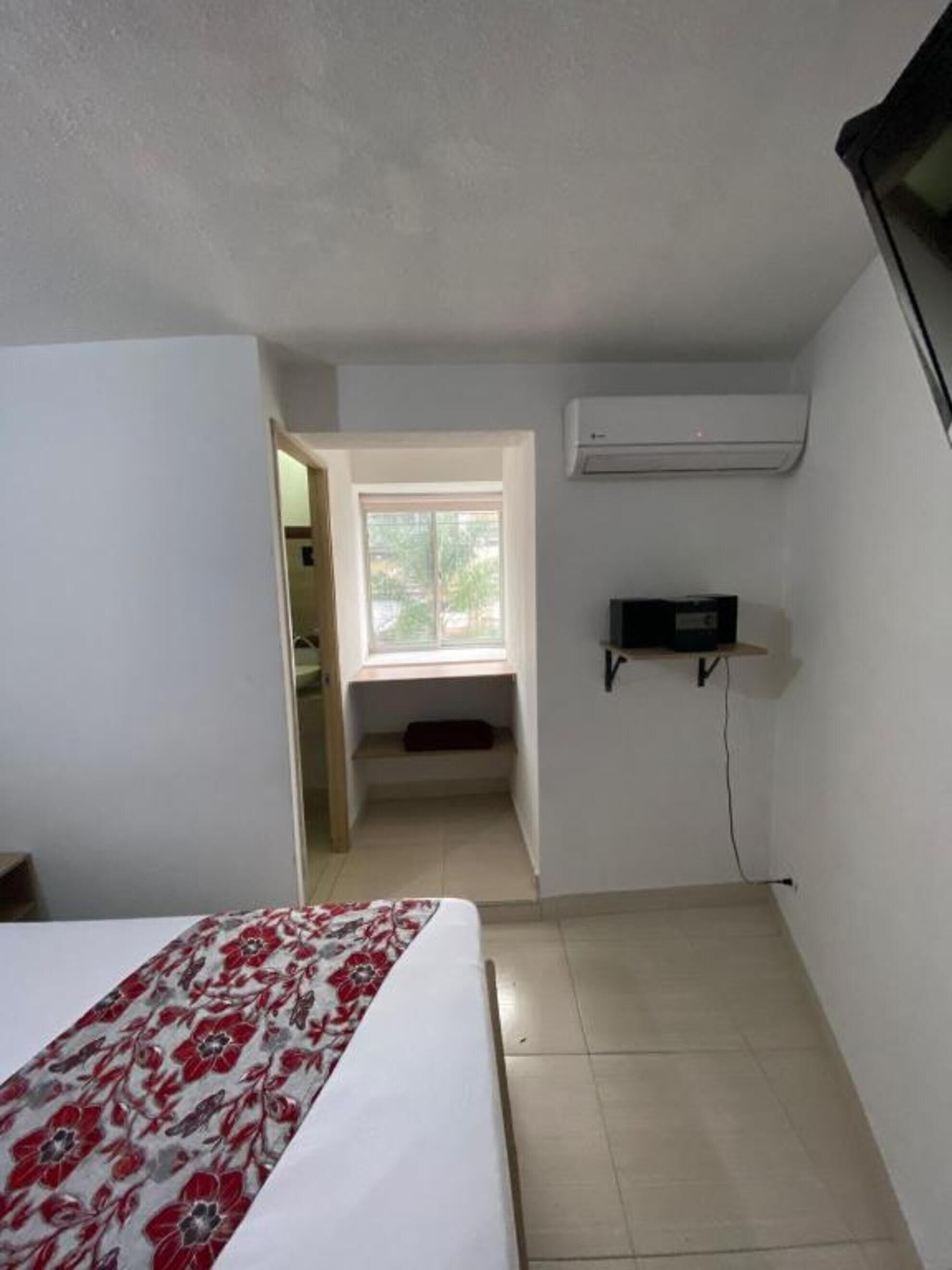 A small, clean room with a bed, a window, and an air conditioning unit.