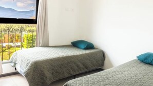 A room with two beds, a window with a view of greenery and mountains, and a balcony with a metal railing. - *Beautiful colonial house* in Antigua Guatemala (Alotenango)