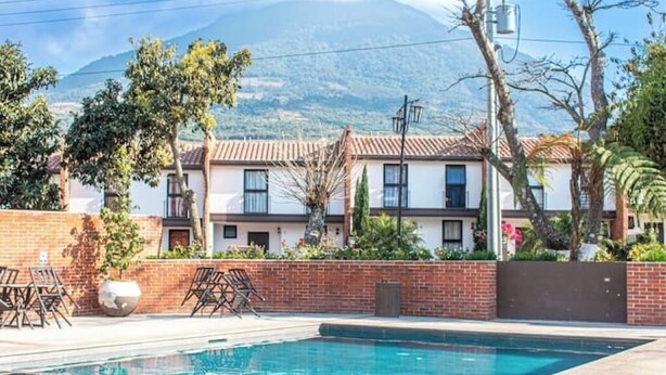 A swimming pool with a view of a mountain range, surrounded by a brick wall and a row of houses. - *Beautiful colonial house* in Antigua Guatemala (Alotenango)