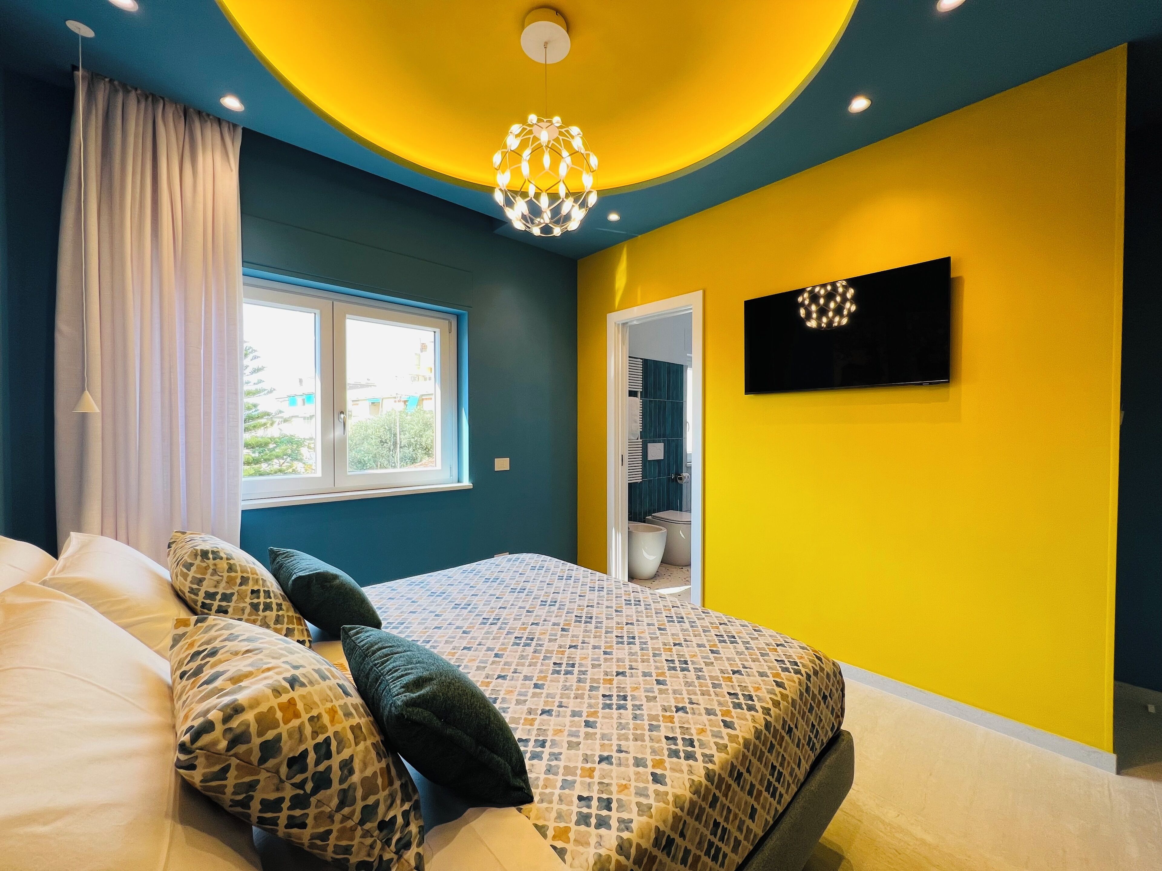 Ein Schlafzimmer mit Bett, Fenster, Fernseher und angrenzendem Badezimmer.