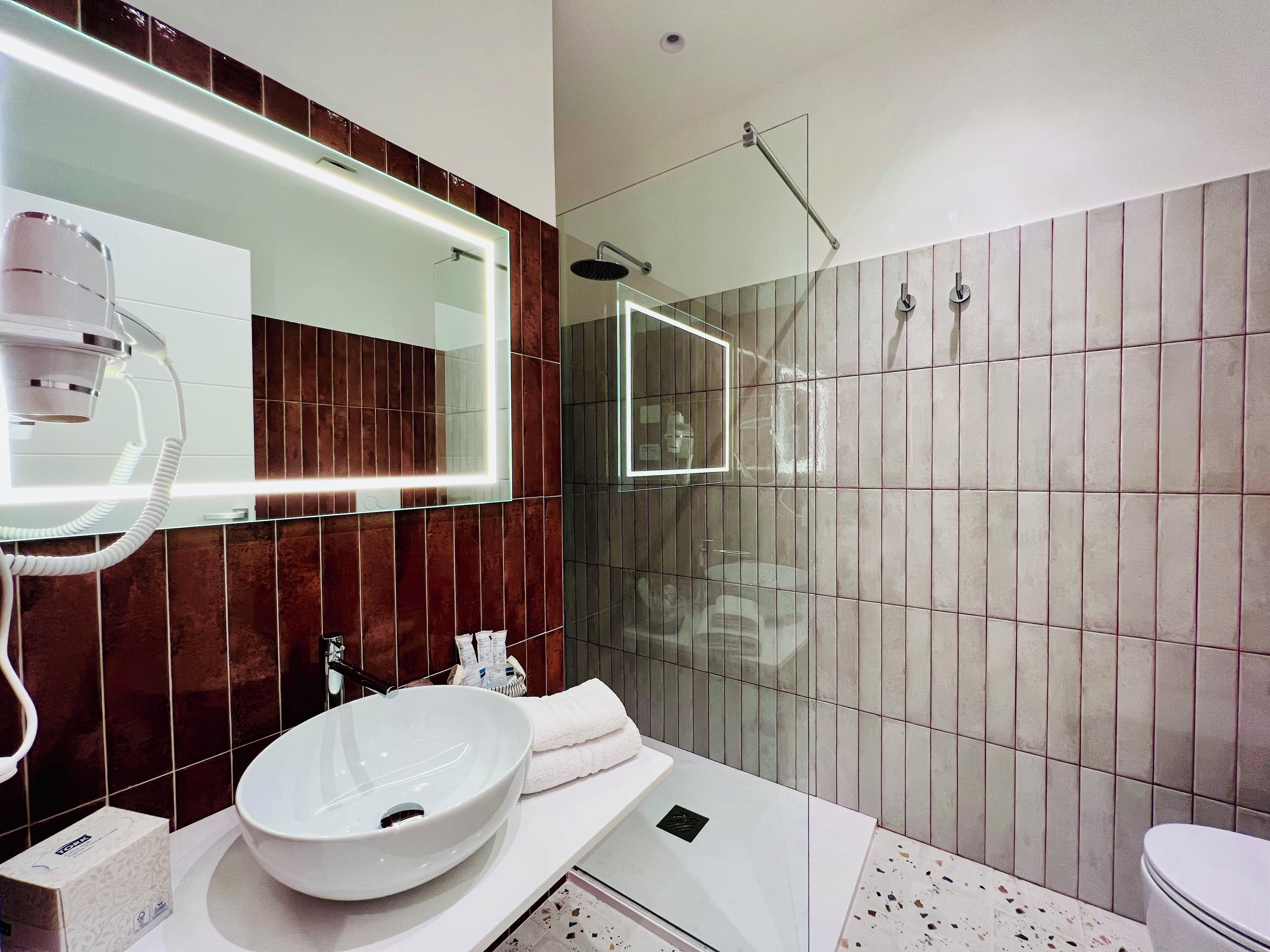 A modern bathroom with a large mirror, a vessel sink, a handheld showerhead, and a toilet.